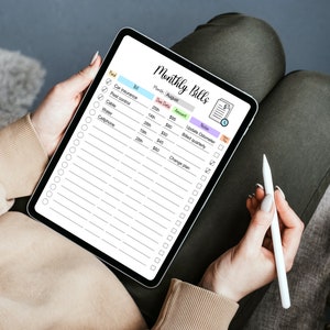 May include: A digital tablet with a monthly bills checklist for August. The checklist includes a column for the bill, due date, amount, and notes. The tablet is on a person's lap and a stylus is being used to check off items on the list.