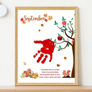 May include: A framed print with a red handprint on a tree with green leaves and red apples. The text reads 'September' and 'In September's reign, fall descends, Leaves of gold, nature amends. Crisp air whispers through the trees, A sight of beauty, nature's masterpiece.'