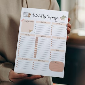 May include: A white printable work day organiser with a brown and white coffee cup, a calendar, and a potted plant illustration. The organiser has sections for priorities, deadlines, to do list, schedule, calls, emails, meetings, reminders, and notes.