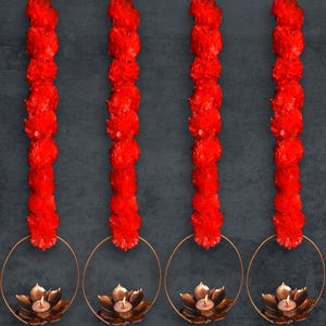 May include: Four red flower garlands hang from gold hoops with a small candle in each hoop. The candles are in the shape of a lotus flower.