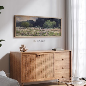 May include: A wooden cabinet with two doors and three drawers. The doors have a woven cane pattern. The cabinet is sitting on a wooden floor in front of a white wall. There is a painting of a landscape above the cabinet.