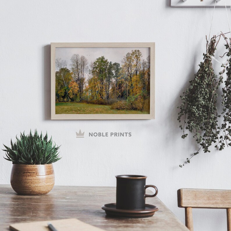 Op de afbeelding: Een ingelijste foto van een boslandschap met bomen in verschillende tinten groen en geel. De bomen bevinden zich op de achtergrond en er is een grasveld op de voorgrond. De foto hangt aan een witte muur.