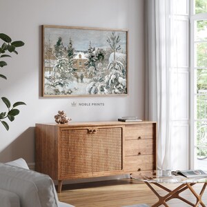 May include: A framed winter landscape painting hangs above a wooden cabinet. The artwork depicts a snow-covered scene with trees and a building. The cabinet has a woven door panel and three drawers. A glass-topped coffee table and a white curtain are also visible.
