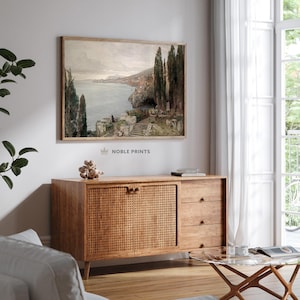 May include: A vintage-style painting of a coastal landscape with a stone staircase leading down to the water. The painting is framed in a light wood frame and hangs on a white wall.