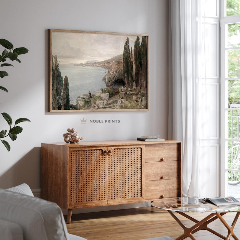 May include: A vintage-style painting of a coastal landscape with a stone staircase leading down to the water. The painting is framed in a light wood frame and hangs on a white wall.