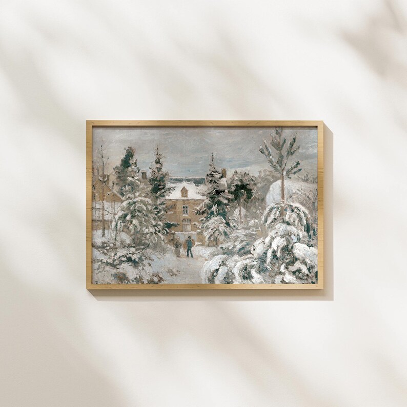 May include: A framed winter landscape painting. The artwork depicts a snow-covered scene with a building, trees, and figures. The color palette is muted, with shades of gray, white, and brown. The frame is a light wood color.
