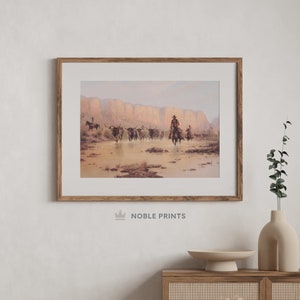 May include: A framed print of a painting depicting a cowboy riding a horse through a desert landscape with a herd of cattle. The scene is set against a backdrop of red rock cliffs and a clear blue sky.