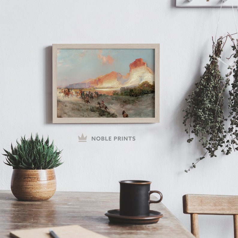Puede incluir: Una pintura enmarcada que representa una escena de paisaje con un grupo de personas a caballo cabalgando por un valle con una gran formaci&oacute;n rocosa en el fondo. El cielo es de un azul suave con nubes rosadas y naranjas. La pintura est&aacute; en un marco de madera claro.