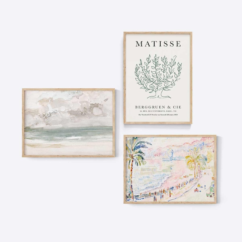 May include: Three framed art prints with a beach scene, a tree, and a palm tree. The beach scene is a watercolor painting with a cloudy sky and a light blue ocean. The tree is a line drawing of a green tree with the text "MATISSE" and "BERGGREEN & CIE" below it. The palm tree is a colorful painting of a beach scene with palm trees and people walking along the shore.