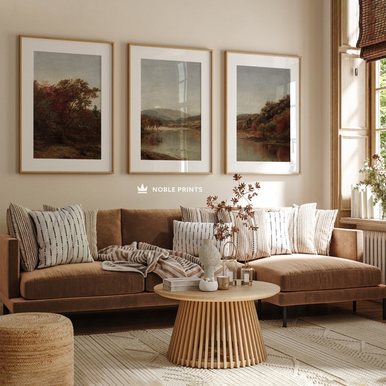 May include: A brown sectional sofa with throw pillows and a blanket, a wooden coffee table, and a woven ottoman in front of a wall with three framed landscape paintings. The paintings are in a light brown frame and feature a lake scene with trees and mountains.