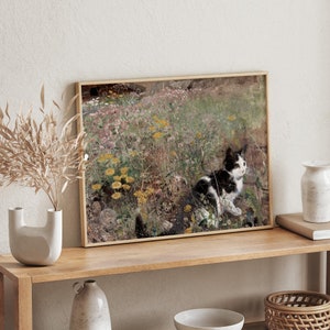 May include: A framed painting of a black and white cat sitting in a field of wildflowers. The cat is looking to the right of the image. The painting is in a light wood frame.