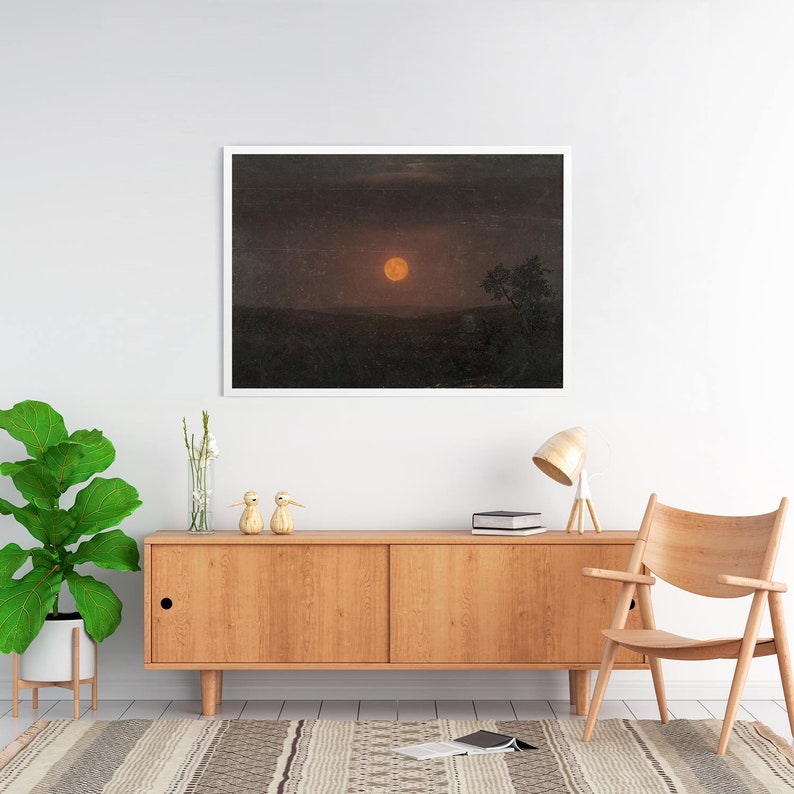 May include: A framed print of a landscape with a large, orange moon in the sky. The moon is surrounded by dark clouds and a silhouette of a tree is visible in the distance.