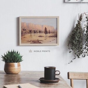 May include: A framed print of a painting depicting a group of cowboys on horseback driving a herd of cattle through a shallow river. The scene is set against a backdrop of red rock cliffs.