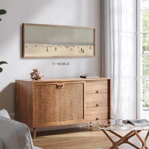 Può includere: Un mobile in legno con una parte anteriore in rattan intrecciato, tre cassetti e un dipinto che raffigura una scena di spiaggia sopra. Il mobile ha una finitura in legno chiaro e si trova su un pavimento in legno.