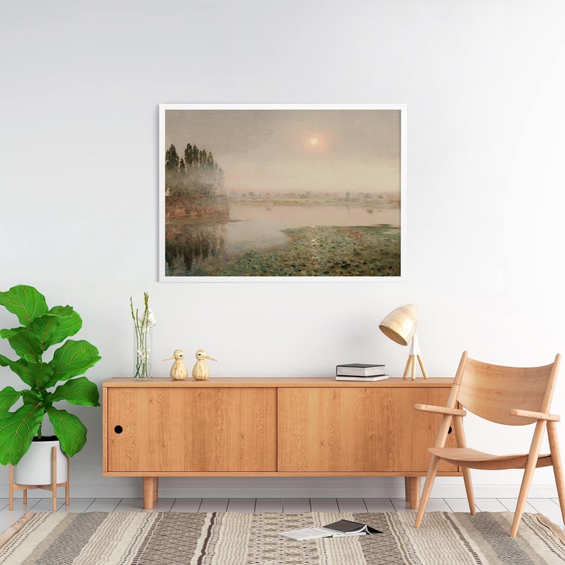 May include: A framed landscape painting depicting a misty lake scene with a group of trees on a small island in the foreground. The sun is shining brightly in the sky, casting a warm glow over the water.