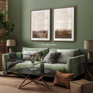 May include: A green velvet sofa with throw pillows and a blanket, a black coffee table with a vase of dried flowers, and two framed landscape prints on a sage green wall.
