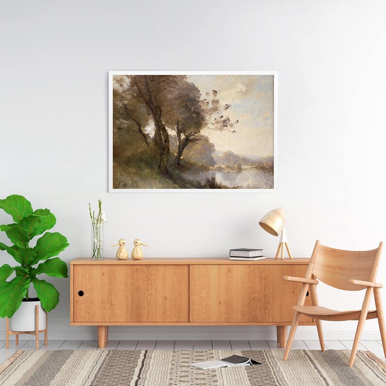 Puede incluir: Una pintura de paisaje enmarcada representa &aacute;rboles cerca de un cuerpo de agua. La obra de arte, en un marco blanco, presenta tonos apagados de marr&oacute;n, verde y beige. La pintura cuelga sobre un mueble de madera con una l&aacute;mpara, una silla y objetos decorativos.