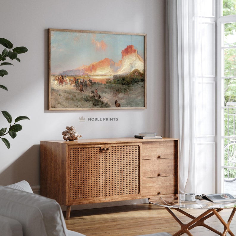 Puede incluir: Una pintura vintage que representa a un grupo de personas a caballo cabalgando por un paisaje des&eacute;rtico. La pintura presenta un cielo dram&aacute;tico con una puesta de sol naranja brillante y una gran formaci&oacute;n rocosa en el fondo. La pintura est&aacute; enmarcada en un marco de madera simple.