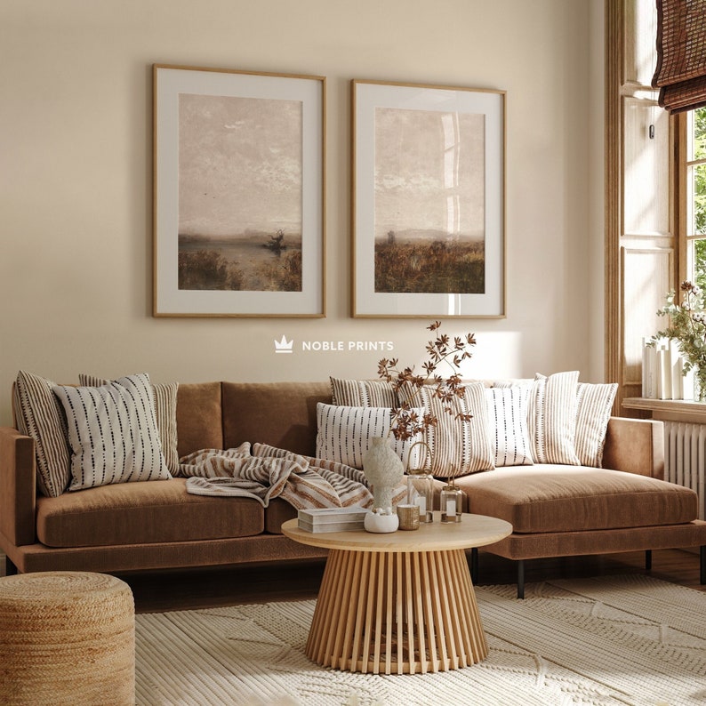 May include: A brown sectional sofa with a wooden coffee table and two framed landscape paintings on the wall. The sofa has a throw blanket and pillows with a white and black geometric pattern. The coffee table has a vase with dried flowers and candles.