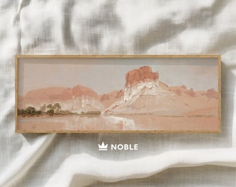 May include: A framed landscape painting depicting a desert scene with a river flowing through a canyon. The painting features a light pink and brown color palette with a soft, hazy atmosphere.