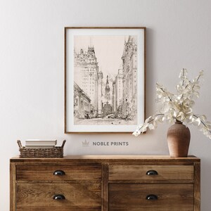 May include: A black and white line drawing of a city street with tall buildings on either side. The drawing is framed in a light wood frame and is hanging on a white wall.