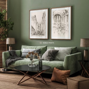 May include: Two black and white framed illustrations of cityscapes hang on a sage green wall above a green velvet sofa. The sofa has a black coffee table in front of it and a brown throw pillow on the floor.