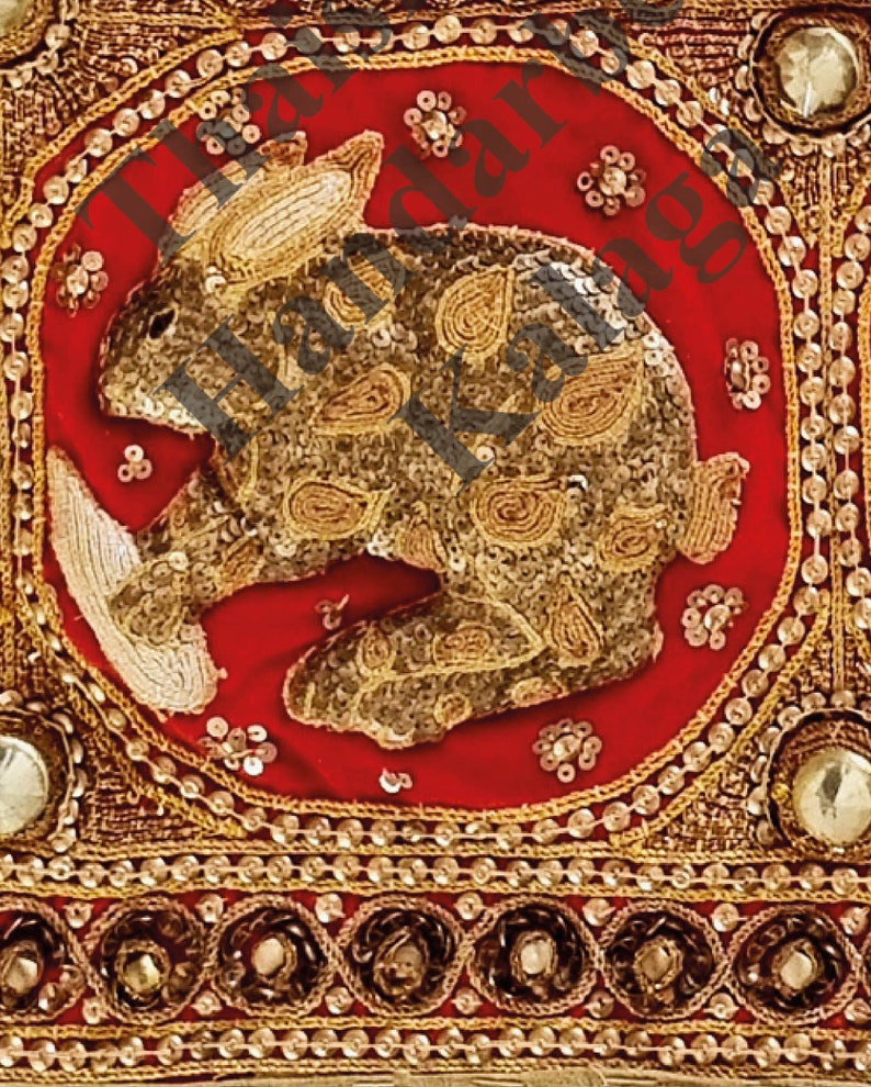 May include: A red fabric square with a gold embroidered rabbit design. The rabbit is surrounded by a gold border with small gold beads. The fabric has a gold and red border with small gold beads.