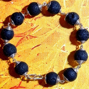 May include: A black lava rock bracelet with silver wire wrapping each bead. The bracelet is made of 10 beads and is approximately 8 inches in length.