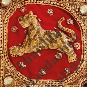 May include: A gold embroidered tiger on a red velvet background with gold trim and sequins. The tiger is facing left and has a curled tail.