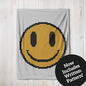 May include: A crochet blanket featuring a large yellow smiley face design. The blanket is made with a textured stitch and has a white background. The text "Now Includes Written Pattern!" is on a black circle in the bottom right corner of the image.