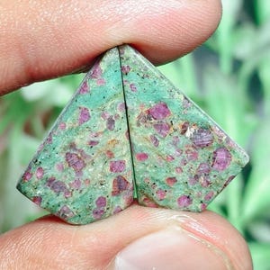 Pode incluir: Duas pedras preciosas polidas de formato triangular com uma cor base verde menta vibrante e inclusões irregulares de magenta profundo e vermelho escuro espalhadas por toda a superfície, exibindo uma textura natural salpicada.