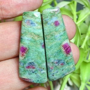 Peut inclure: Deux pierres précieuses polies de forme trapézoïdale présentant une base vert vif avec des inclusions distinctes de dépôts minéraux magenta-rose profond et bleu foncé sur toute la surface lisse et brillante de chaque pierre.