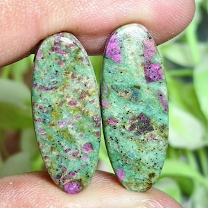 Peut inclure: Deux cabochons ovales en rubis sur zoïsite, présentant une base de couleur vert vif avec des inclusions de rubis magenta-rose opaques dispersées et des taches minérales noires sombres sur toutes les surfaces polies, lisses et arrondies.