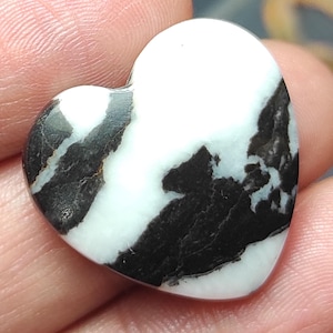 Puede incluir: Una piedra en forma de corazón con un llamativo diseño en blanco y negro. La superficie pulida muestra vetas negras sobre un fondo blanco. La forma de corazón es lisa y simétrica, ideal como objeto decorativo.