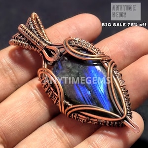 Puede incluir: Un colgante envuelto en alambre de cobre con una piedra preciosa de labradorita azul. El colgante tiene un diseño único e intrincado y es una hermosa pieza de joyería.