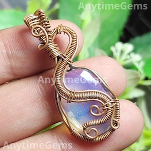 May include: A copper wire-wrapped pendant with an iridescent, oval gemstone. The wire is intricately woven around the stone, creating a unique design. The pendant is held in a hand, highlighting the craftsmanship. The pendant is a piece of jewellery.