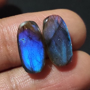 May include: Two oval-shaped labradorite gemstones with iridescent blue and grey hues.