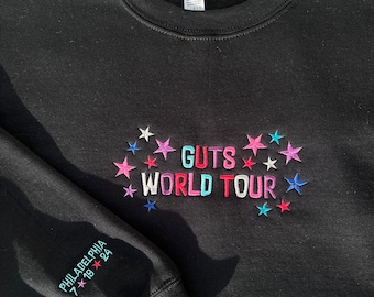 May include: Black sweatshirt with the text "GUTS WORLD TOUR" embroidered in colorful letters surrounded by stars. The left sleeve has the text "PHILADELPHIA 7.18.24" embroidered in white.