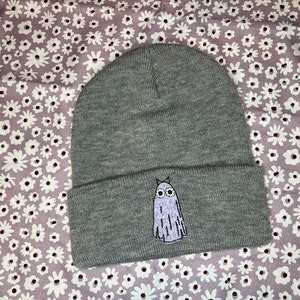 Pode incluir: Bon&eacute; cinza com um fantasma branco bordado na frente. O fantasma tem olhos grandes e uma pequena boca.