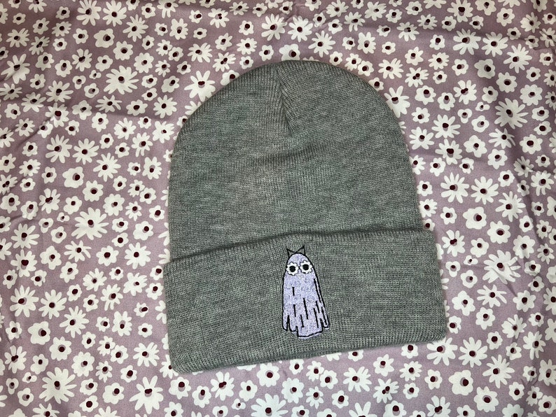 Pode incluir: Bon&eacute; cinza com um fantasma branco bordado na frente. O fantasma tem olhos grandes e uma pequena boca.