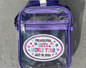 Puede incluir: Bolso transparente de plástico morado con cierre de cremallera y un parche que dice "Philadelphia Guts World Tour July 19, 2024" con estrellas alrededor del texto.