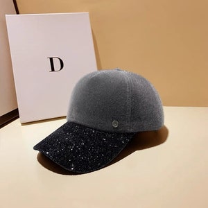 May include: A gray and black baseball cap with a sparkly black brim. The cap is made of a soft, fuzzy material.