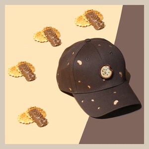 May include: A brown baseball cap with a cookie design on the front. The cap has a brown brim and a brown adjustable strap. The cap is surrounded by four small, round, brown and tan cookies.