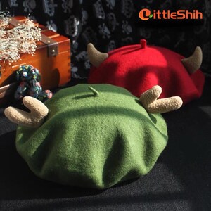 May include: Two felt berets with reindeer antlers. One beret is green and the other is red.