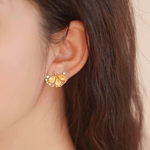 May include: Gold tone earrings with a ginkgo leaf design. The leaves are textured and have small clear stones.