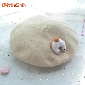 May include: A beige beret with a whimsical dog butt applique. The beret is made of a soft, felt-like material. The dog butt is white with a brown patch and black paws. The LittleShih logo is in the upper left corner.