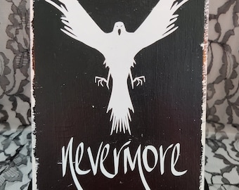 May include: A black wooden sign with white paint. The sign features a white silhouette of a bird with outstretched wings and the text "Nevermore".