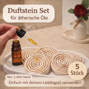 Könnte beinhalten: Ein Set aus fünf spiralförmigen Aromasteinen auf einem weißen Tablett. Eine Hand hält eine Pipette, die Öl aus einer kleinen braunen Flasche auf die Steine tropft. Der Text lautet "Duftstein Set für ätherische Öle".