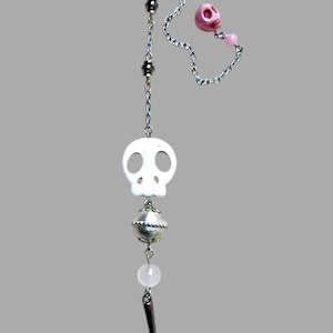 Puede incluir: Una cadena plateada con un colgante de calavera blanca, una cuenta plateada, un dije de calavera rosa y un dije de punta negro. Joyería de estilo gótico con motivos de calaveras.