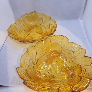 May include: Two amber glass bowls with a leaf design. The bowls are empty and have a slightly rippled surface.